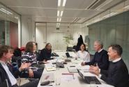 EEAC baord and secretarit members sit in a well-lit conference room around a table. Papers and laptops in front of them, all dicussing and smiling.